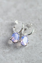 Silver hoop earrings with purple gemstones on a gray surface