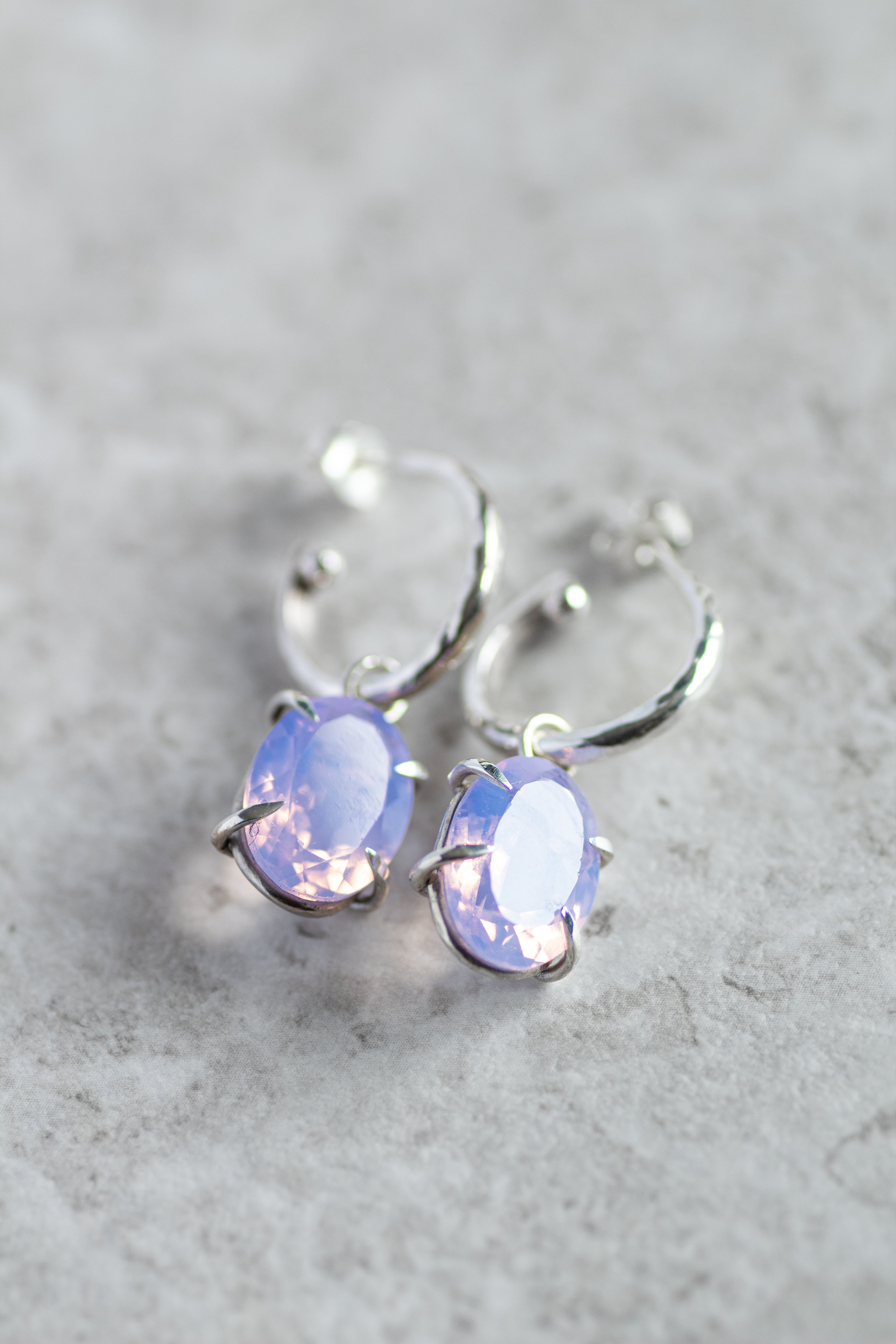 Silver hoop earrings with purple gemstones on a gray surface