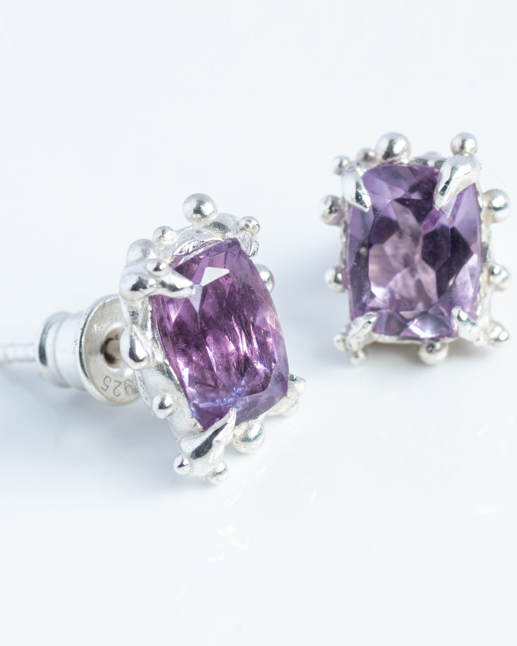 Pair of silver earrings with purple gemstones on a white background