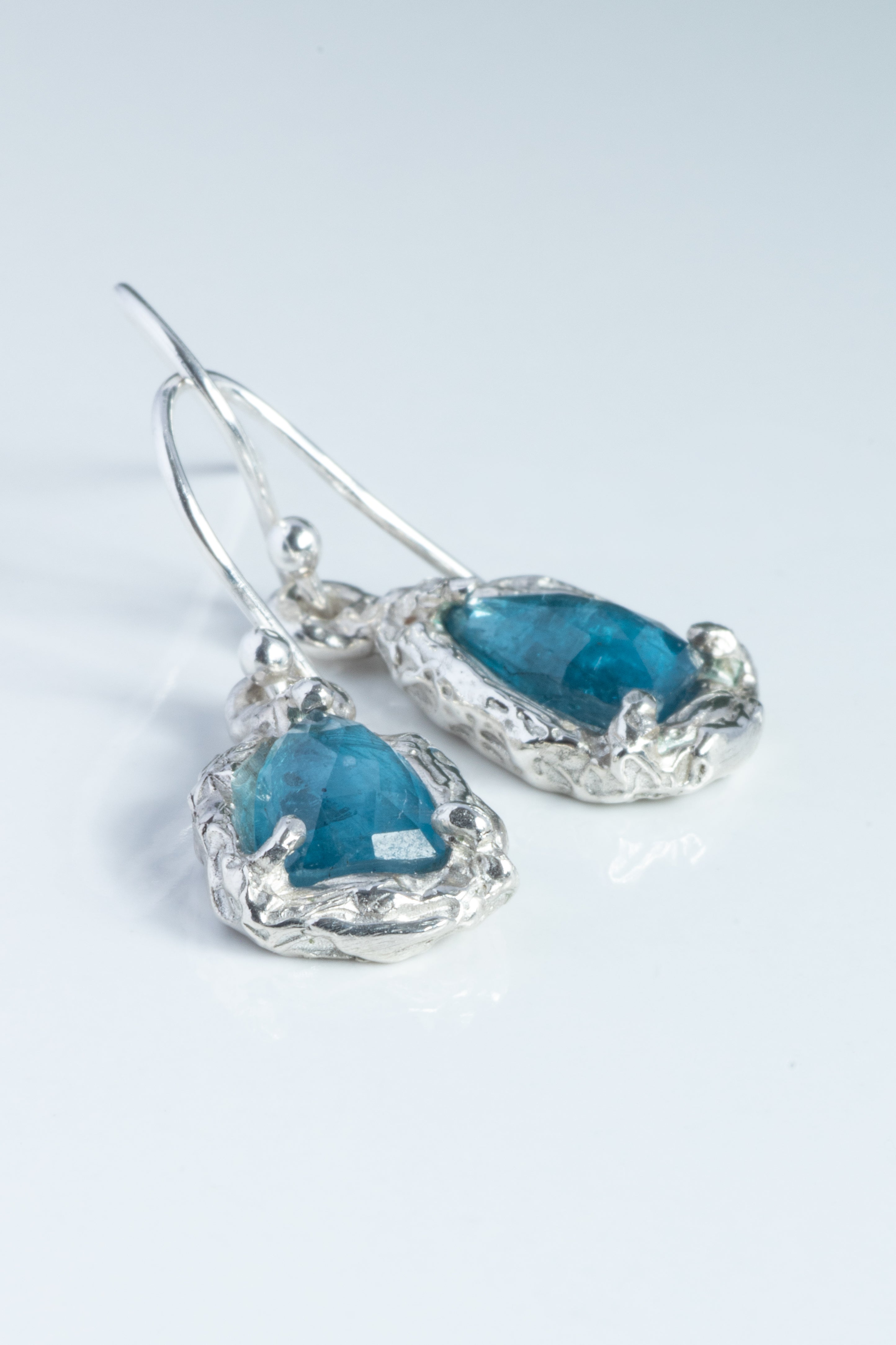 Teardrop-shaped blue gemstone earrings with silver settings on a light gray background