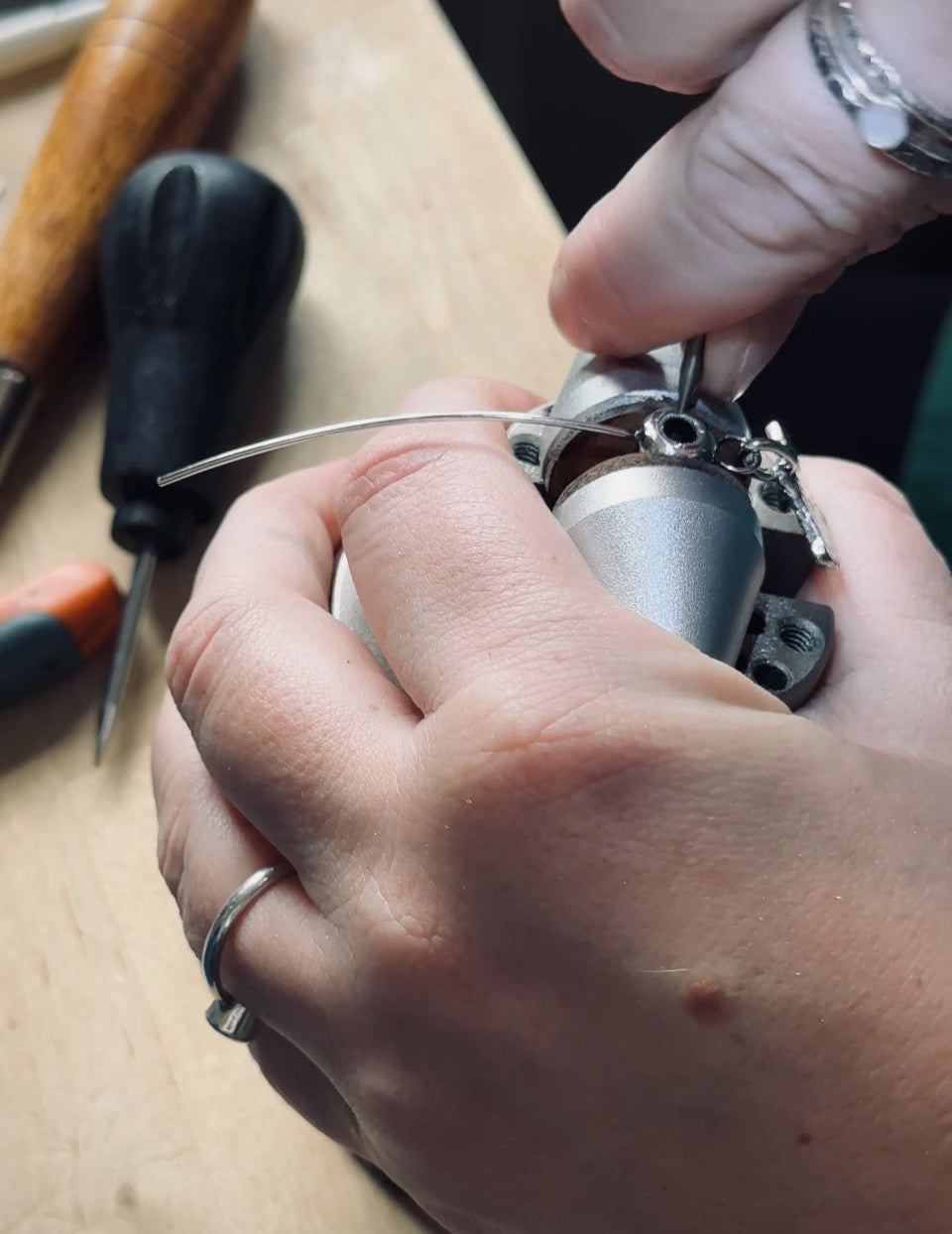 Close-up of hands working on a ball vice device with silversmithing tools in the background.